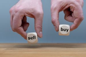 Руки держат два кубика со словами «продать» и «купить».