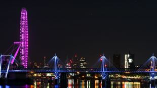 «Лондонский глаз» светился розовым светом на берегу Темзы ночью, с отражениями городского пейзажа на воде. 