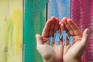 Бумажная семья в руках на деревянных цветном фоне 