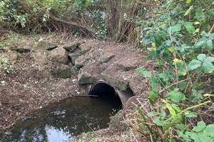 Небольшой туннель под берегом, по которому течет вода.