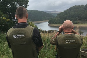Два офицера Агентства по охране окружающей среды проверяют в бинокль отдаленный берег реки.