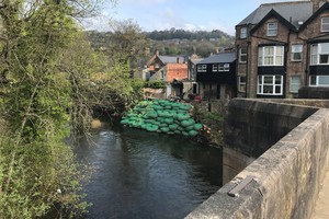 Зеленые мешки с камнями, сложенные у реки перед домами