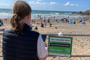 Молодая женщина использует свой мобильный телефон для сканирования QR-кода на вывеске на фоне оживленного пляжа.