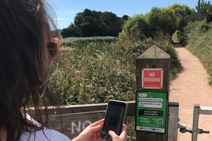 Женщина с помощью мобильного телефона сканирует QR-код на столбе забора