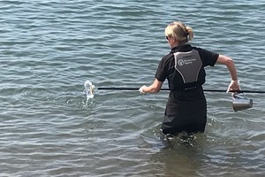Женщина в спасательном жилете по пояс в морской воде берет пробу воды для купания